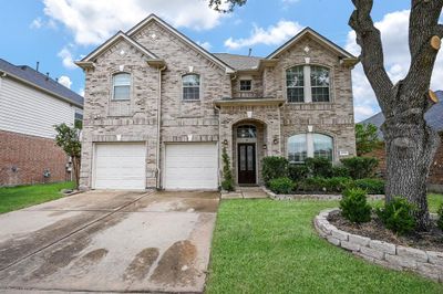 This is a two-story home featuring a double garage, arched entryway, and landscaped front yard with a mature tree, offering a classic appeal. | Image 2