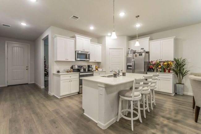 Kitchen featuring stainless steel appliances, a sink, dark wood-style floors, a kitchen island with sink, and white cabinetry | Image 7
