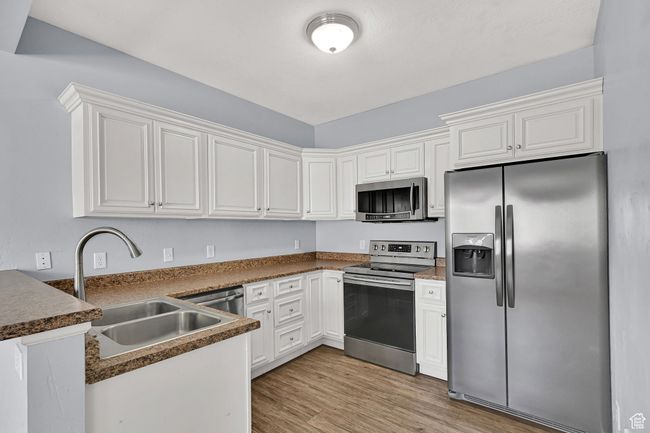 Kitchen with appliances with stainless steel finishes, a peninsula, light wood-style floors, white cabinetry, and dark countertops | Image 6