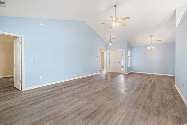 Unfurnished living room featuring ceiling fan, a chandelier, wood finished floors, and high vaulted ceiling | Image 9
