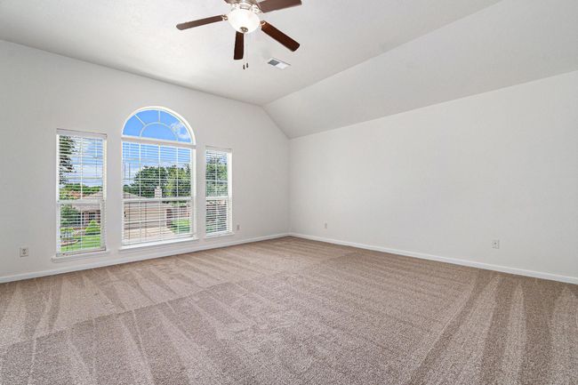 Spacious, primary bedroom with neutral carpet, large arched window offering plenty of natural light, and a ceiling fan. | Image 11