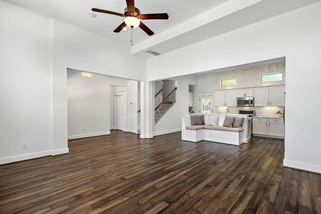 Living area with dark wood-style floors, a high ceiling, ceiling fan, stairs, and visible vents | Image 8