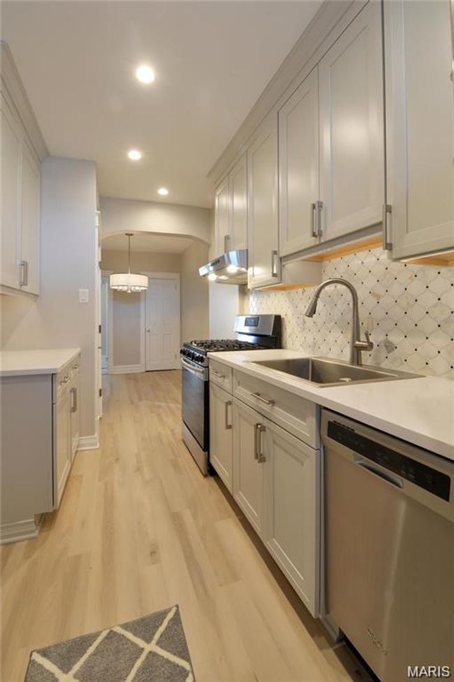 Kitchen with stainless steel appliances, under cabinet range hood, light wood finished floors, backsplash, and recessed lighting | Image 11