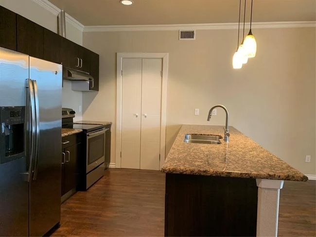 Kitchen with appliances with stainless steel finishes, a peninsula, under cabinet range hood, dark wood finished floors, and crown molding | Image 18