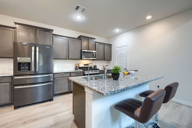 Kitchen featuring appliances with stainless steel finishes, light wood-style flooring, light stone countertops, a kitchen bar, and a sink | Image 13