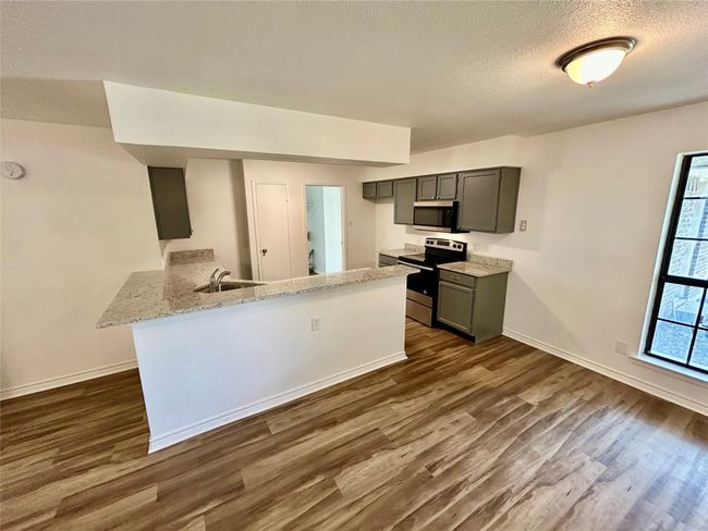 Kitchen featuring appliances with stainless steel finishes, dark wood finished floors, baseboards, a peninsula, and a textured ceiling | Image 7