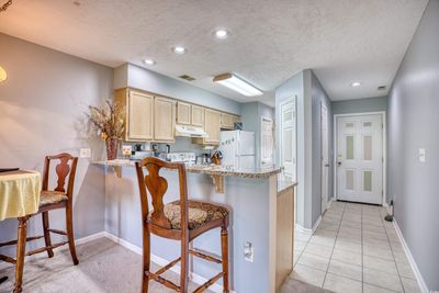 Kitchen with light brown cabinets, kitchen peninsula, light tile patterned floors, a kitchen breakfast bar, and white fridge | Image 3