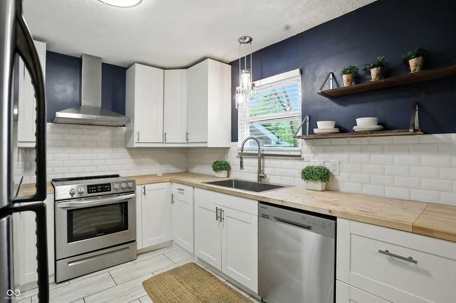 kitchen featuring stainless steel appliances, wall chimney exhaust hood, wood counters, white cabinetry, and tasteful backsplash | Image 5