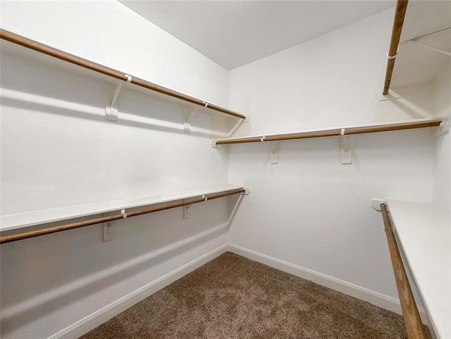 This photo shows a spacious walk-in closet with multiple wooden hanging rods and white shelves, perfect for organizing clothing and accessories. The carpeted floor adds warmth and comfort. | Image 27