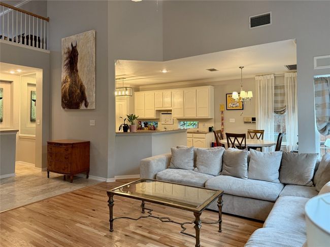 Living area featuring a high ceiling, a chandelier, baseboards, light wood-type flooring, and visible vents | Image 16