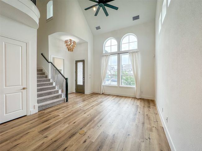 Entrance foyer with a towering ceiling, stairway, wood finished floors, a chandelier, and a ceiling fan | Image 6