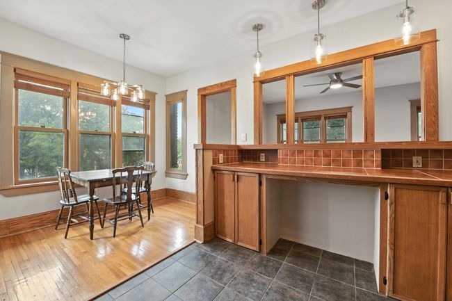 Bright dining area adjacent to kitchen with large windows, hardwood floors, and a view through the original wood pass-through. | Image 15