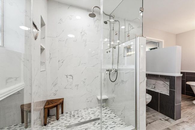 Gorgeous custom glass and tiled walk-in shower with multi shower heads, seating bench and convenient inset shelving | Image 25