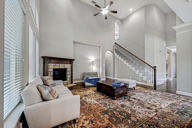 Living area with a high ceiling, wood finished floors, a ceiling fan, stairway, and a fireplace | Image 8