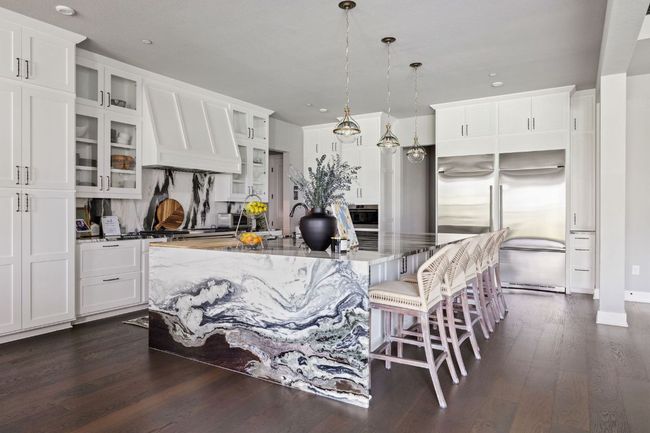Kitchen with stainless steel built in fridge, glass insert cabinets, an island with sink, and dark wood-style flooring | Image 10