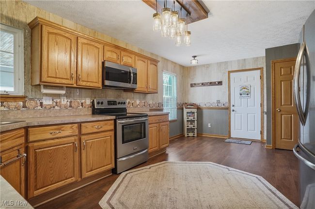 Kitchen with appliances with stainless steel finishes, light countertops, baseboards, an inviting chandelier, and dark wood-style flooring | Image 15