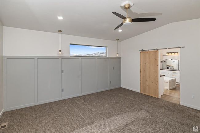 Unfurnished bedroom featuring a barn door, light colored carpet, vaulted ceiling, and ceiling fan | Image 19