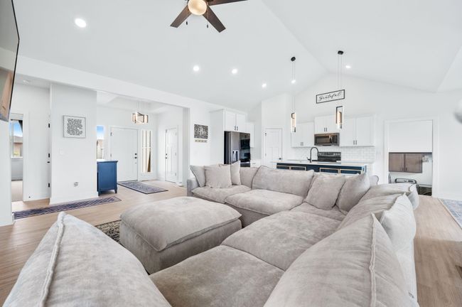 Living room with high vaulted ceiling, ceiling fan, light wood-type flooring, baseboards, and recessed lighting | Image 7