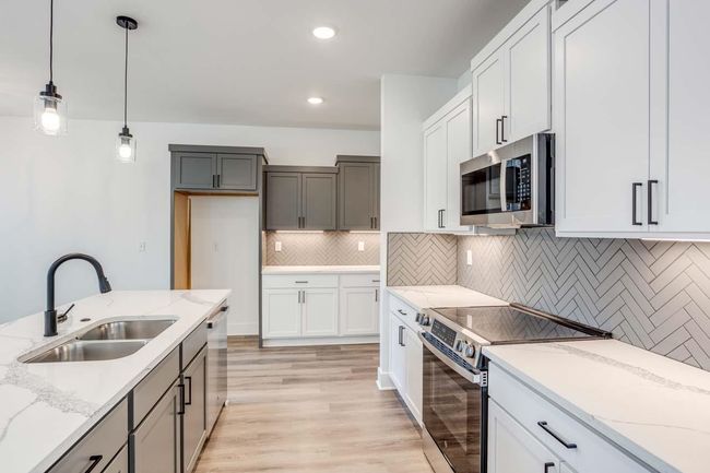 Kitchen with stainless steel appliances, a sink, decorative light fixtures, light stone countertops, and light wood-style floors | Image 9