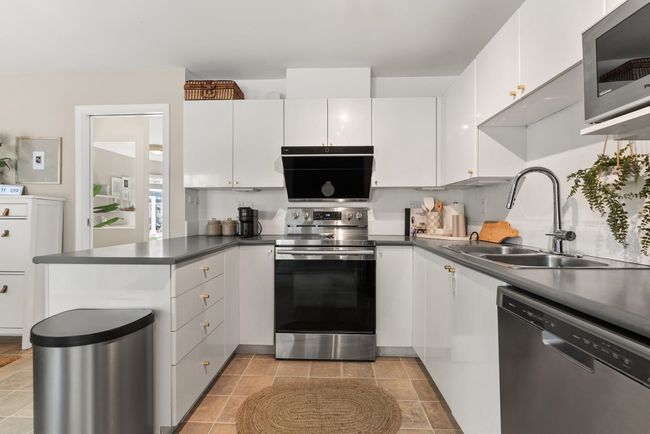 Kitchen featuring stainless steel appliances, a sink, a peninsula, white cabinets, and dark countertops | Image 20
