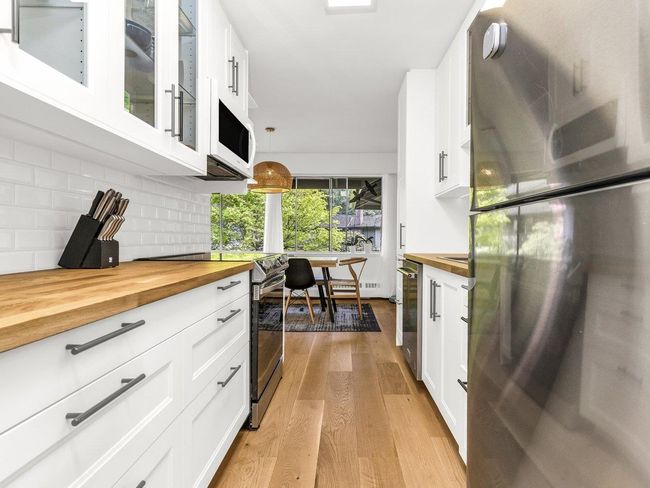 Kitchen with wooden counters, stainless steel appliances, light wood-style floors, backsplash, and glass insert cabinets | Image 4