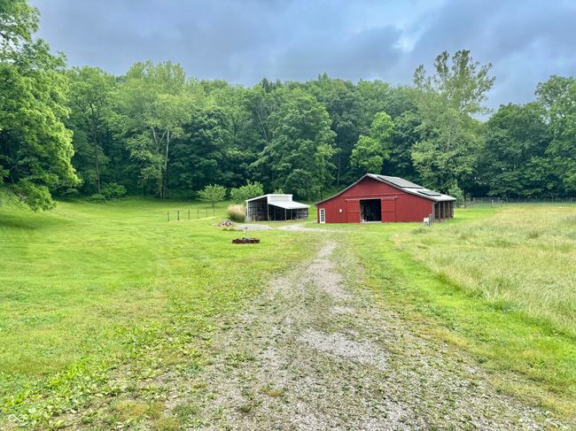 view of green lawn featuring driveway, a wooded view, a pole building, an outbuilding, and a rural view | Image 21