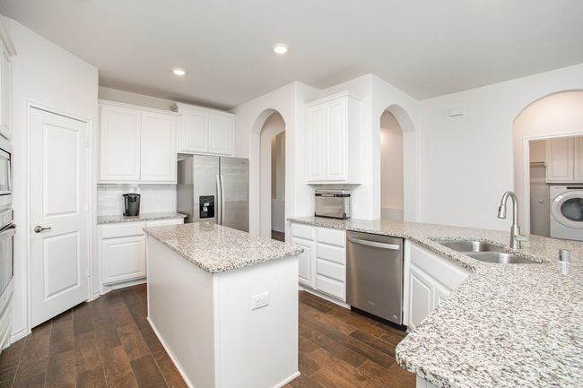Kitchen with appliances with stainless steel finishes, washer / dryer, dark wood finished floors, arched walkways, and a sink | Image 11