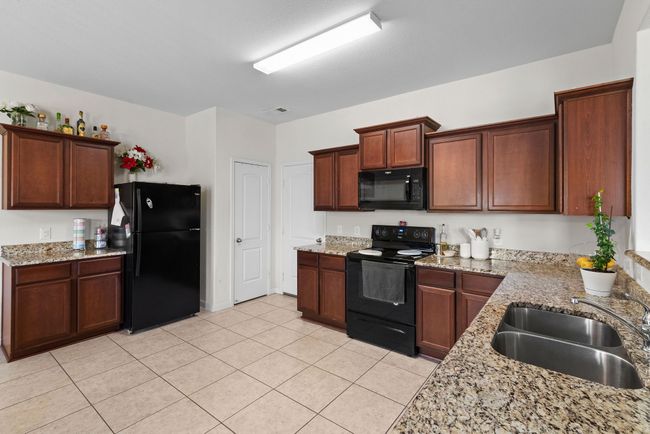 Kitchen featuring light stone countertops, light tile patterned floors, a sink, and black appliances | Image 14