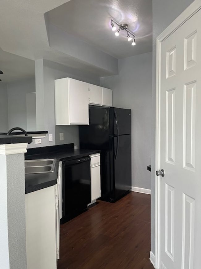 Kitchen with white cabinets, dark wood-style floors, dark countertops, dishwashing machine, and freestanding refrigerator | Image 9