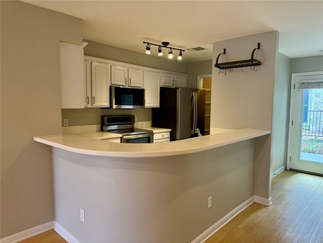 Kitchen with appliances with stainless steel finishes, a peninsula, light wood-style flooring, white cabinetry, and light countertops | Image 5