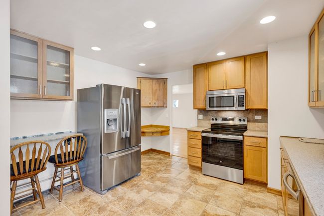 Kitchen featuring tasteful backsplash, glass insert cabinets, light stone counters, stainless steel appliances, and baseboards | Image 10
