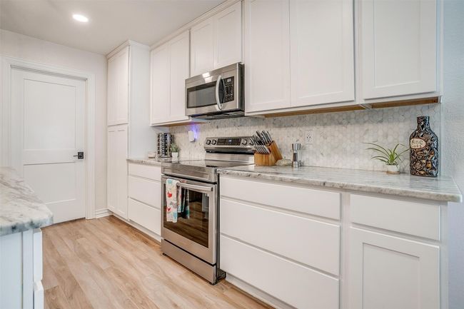 Kitchen with stainless steel appliances, tasteful backsplash, white cabinetry, light wood finished floors, and light marble countertops | Image 17