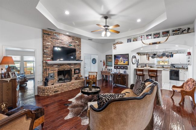 Living room with a tray ceiling, a ceiling fan, visible vents, a brick fireplace, and dark wood-style floors | Image 6