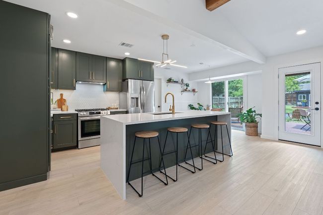 Kitchen with appliances with stainless steel finishes, light wood finished floors, light countertops, decorative backsplash, and a kitchen bar | Image 13