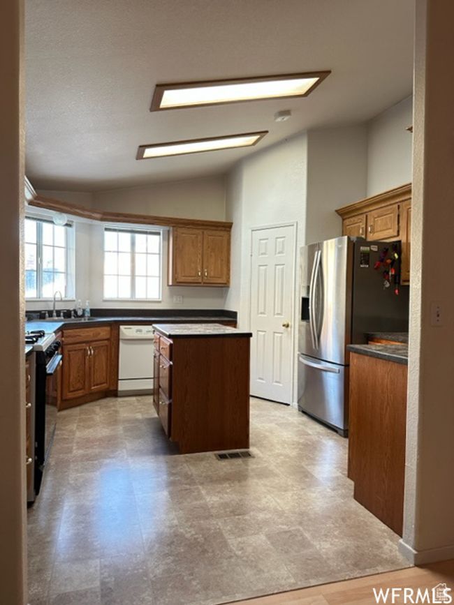 Kitchen featuring stainless steel fridge with ice dispenser, dishwasher, a center island, visible vents, and black range with gas cooktop | Image 31