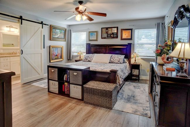 Bedroom with a barn door, light wood-type flooring, ensuite bath, and ceiling fan | Image 17