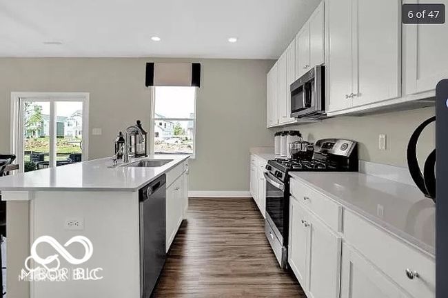 Kitchen with a sink, stainless steel appliances, light countertops, vinyl wood-style flooring, and a kitchen island with sink | Image 4