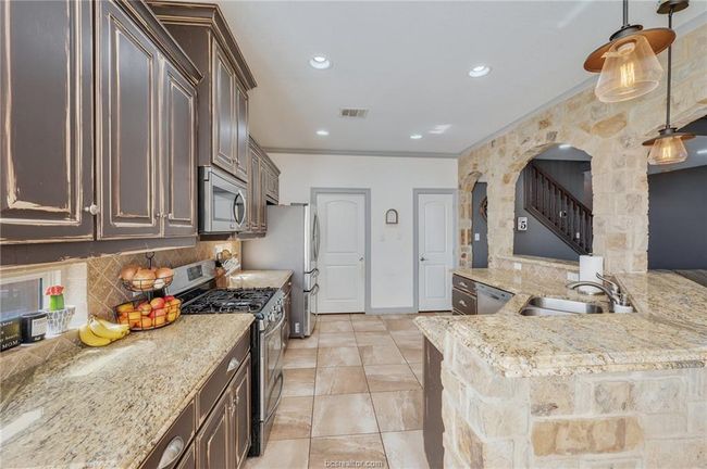 Kitchen featuring stainless steel appliances, dark brown cabinetry, backsplash, crown molding, and light stone countertops | Image 12
