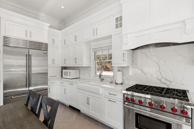 Kitchen with white cabinets, premium appliances, light stone countertops, and backsplash | Image 25