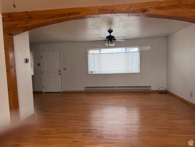Unfurnished living room featuring arched walkways, light wood-type flooring, baseboards, ceiling fan, and a baseboard radiator | Image 11