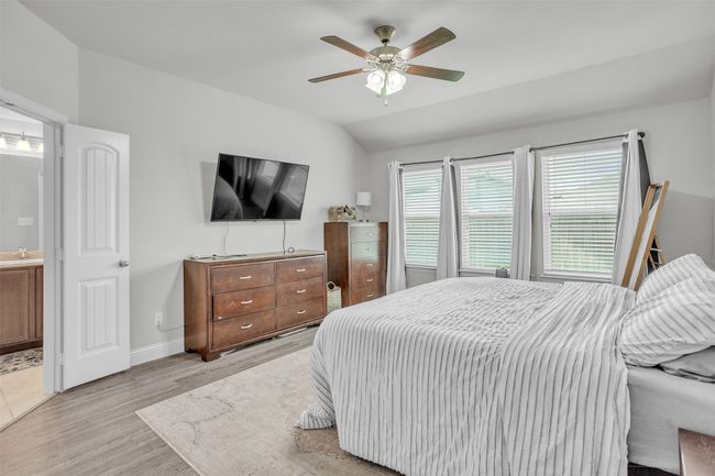 Bedroom with light wood finished floors, vaulted ceiling, connected bathroom, and ceiling fan | Image 15