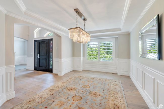 Spare room with a chandelier, a tray ceiling, arched walkways, light wood-style flooring, and wainscoting | Image 8