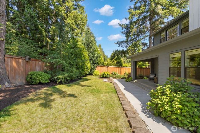 This alternate view of the backyard showcases the seamless blend of manicured lawn, mature privacy trees, and a spacious patio perfect for outdoor dining or lounging. With lush landscaping and room to roam, it’s an ideal setting for peaceful mornings, playful afternoons, or evening gatherings under the stars. | Image 39