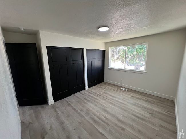 Unfurnished bedroom with a textured ceiling, multiple closets, and light wood-style flooring | Image 19