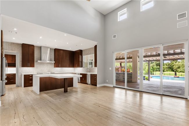Kitchen with wall chimney exhaust hood, a kitchen island, light wood-type flooring, light countertops, and a high ceiling | Image 11