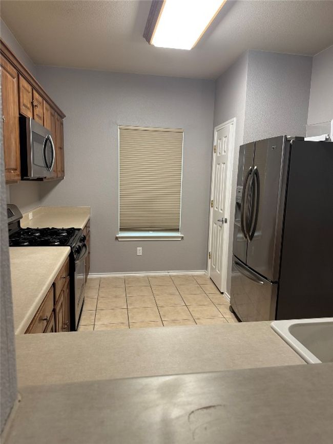 Kitchen featuring stainless steel microwave, gas stove, refrigerator with ice dispenser, brown cabinets, and light countertops | Image 7