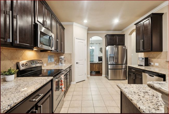 Kitchen featuring stainless steel appliances, arched walkways, light tile patterned floors, ornamental molding, and backsplash | Image 9
