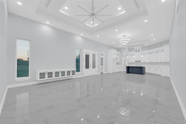 This modern living space features a spacious open floor plan with sleek, high-gloss tile flooring. The room is well-lit with recessed lighting and a contemporary ceiling fan. The kitchen boasts ample cabinetry and a stylish island, perfect for entertaining. Large windows provide natural light and scenic views. | Image 10