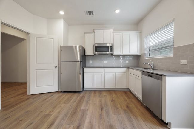 Kitchen with appliances with stainless steel finishes, white cabinetry, tasteful backsplash, light wood-type flooring, and recessed lighting | Image 11