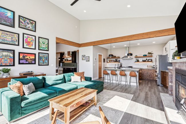 Living area with high vaulted ceiling, a glass covered fireplace, recessed lighting, ceiling fan, and wood finished floors | Image 16
